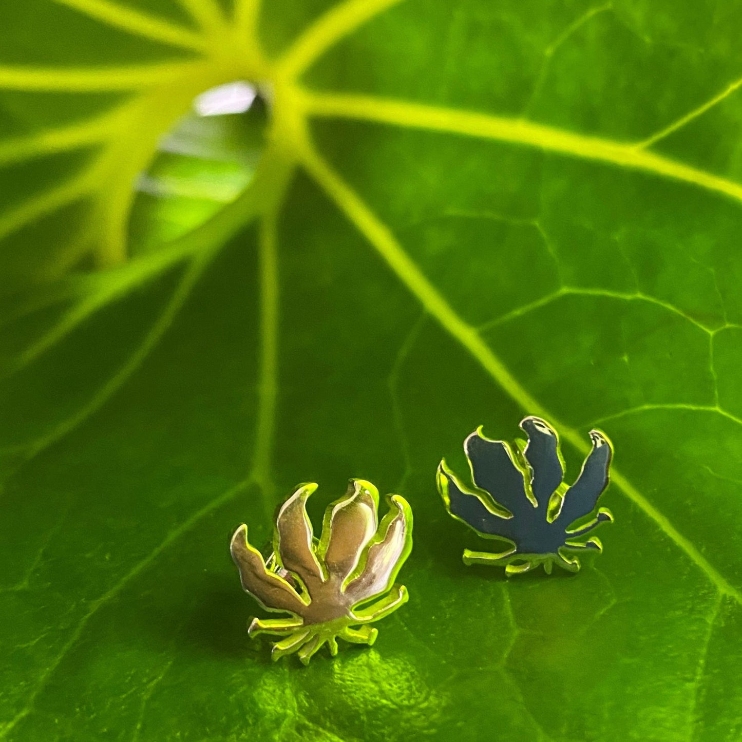 Handcrafted sterling silver Flame Lily stud earrings displayed on a tropical green leaf in natural outdoor light.