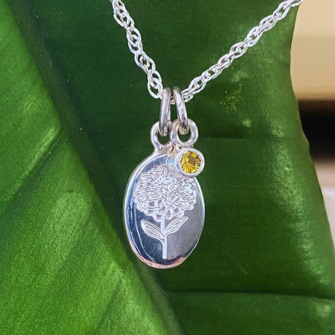 Handcrafted sterling silver birth flower necklace with yellow gemstone displayed on a tropical green leaf.