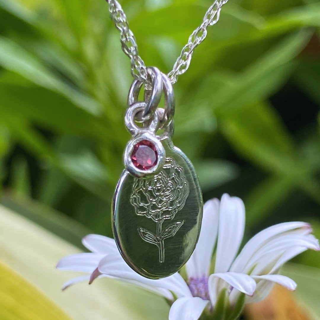 Handcrafted sterling silver birth flower necklace with gemstone displayed on a white daisy.