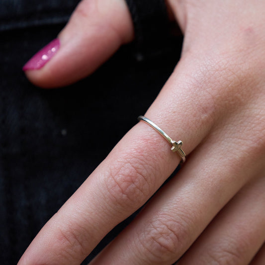Close up of a hand wearing a dainty round silver ring with a tiny cross on it. 