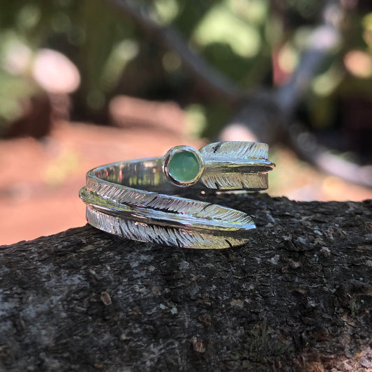 Silver feather ring with a green gemstone sitting on a piece of bark