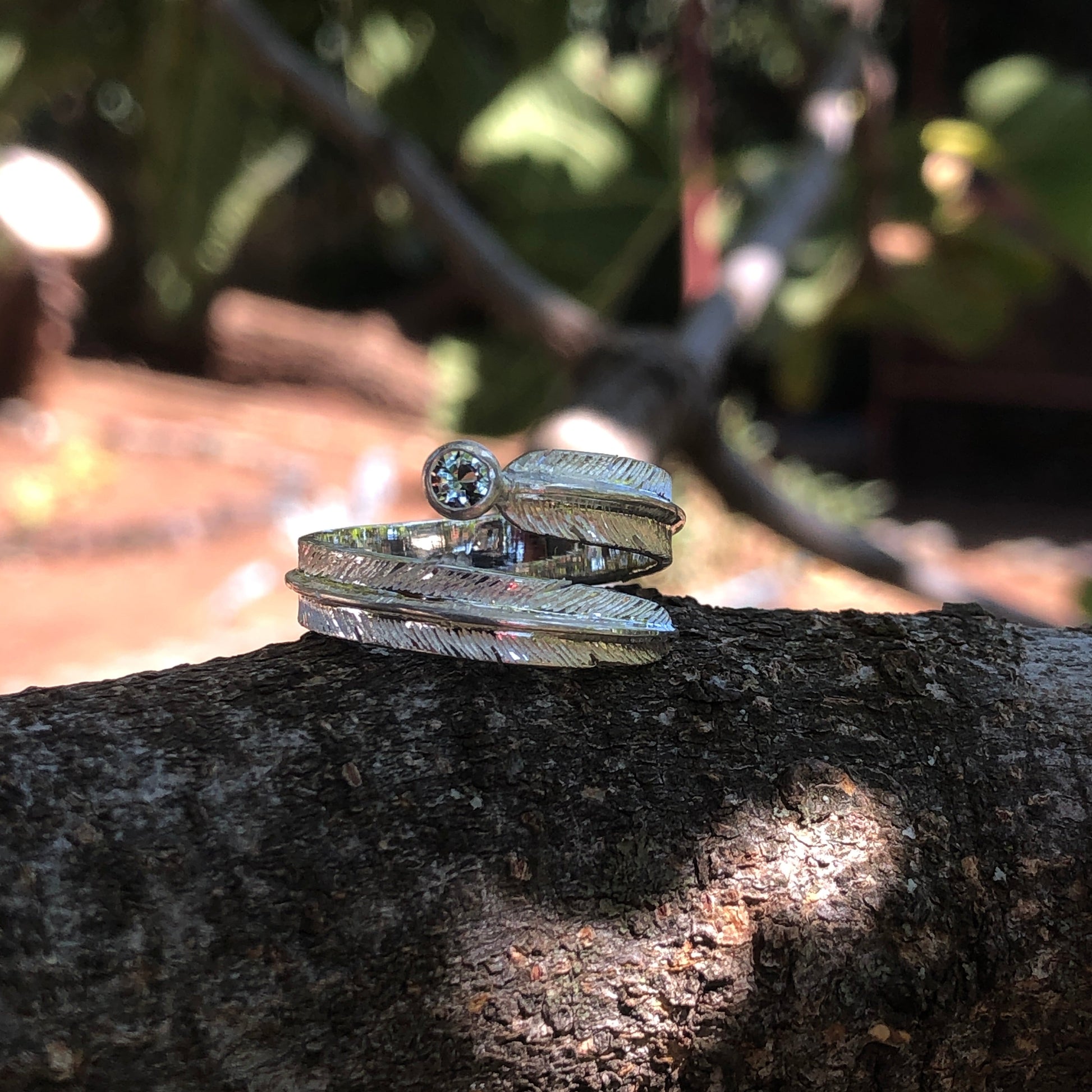 Silver feather ring with a light blue semiprecious gemstone sitting on a branch 