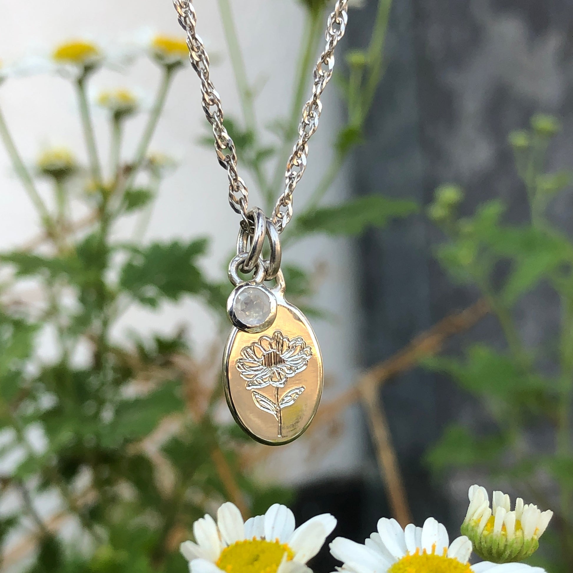 Necklace with a pendant featuring a floral design and a birthstone set on a separate pendant, surrounded by daisies.