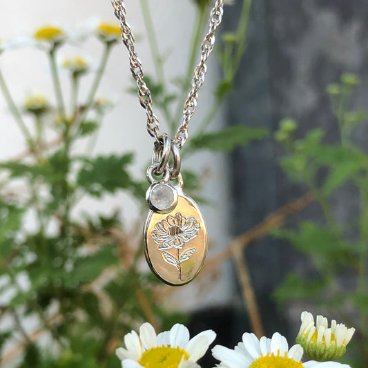 Necklace with a pendant featuring a floral design and a birthstone set on a separate pendant, surrounded by daisies.
