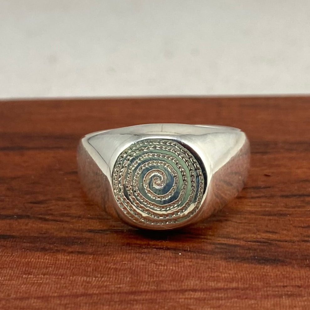 Silver signet ring photographed on a piece of wood.
