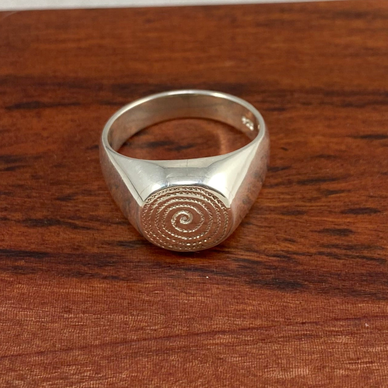 Silver signet ring placed on a piece of reddish wood