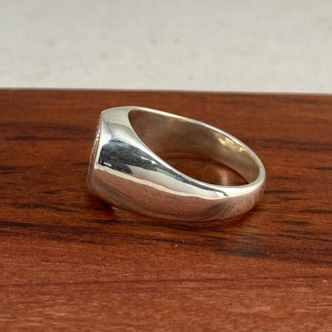 Side view of a silver signet ring on a piece of wood.