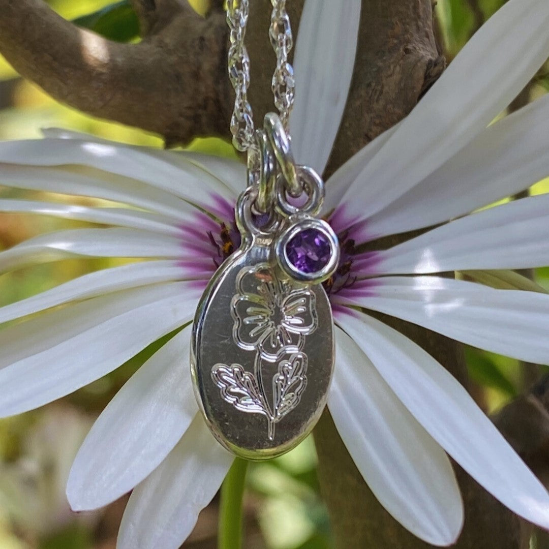 Close-up of a handcrafted sterling silver birth flower necklace with gemstone displayed on a white daisy.