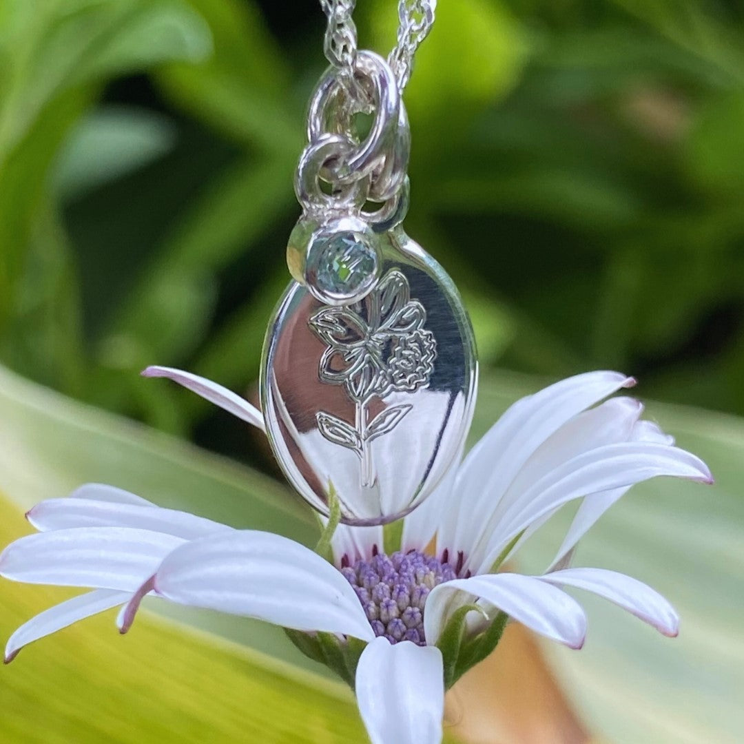 Handcrafted sterling silver birth flower necklace with clear gemstone displayed on a white daisy.