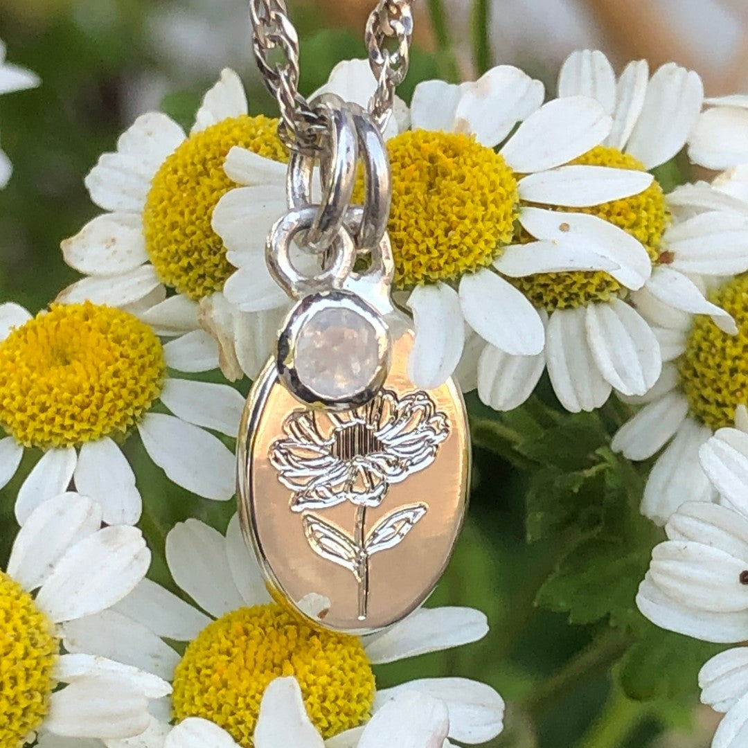 Handcrafted sterling silver birth flower necklace with moonstone displayed among white daisies.