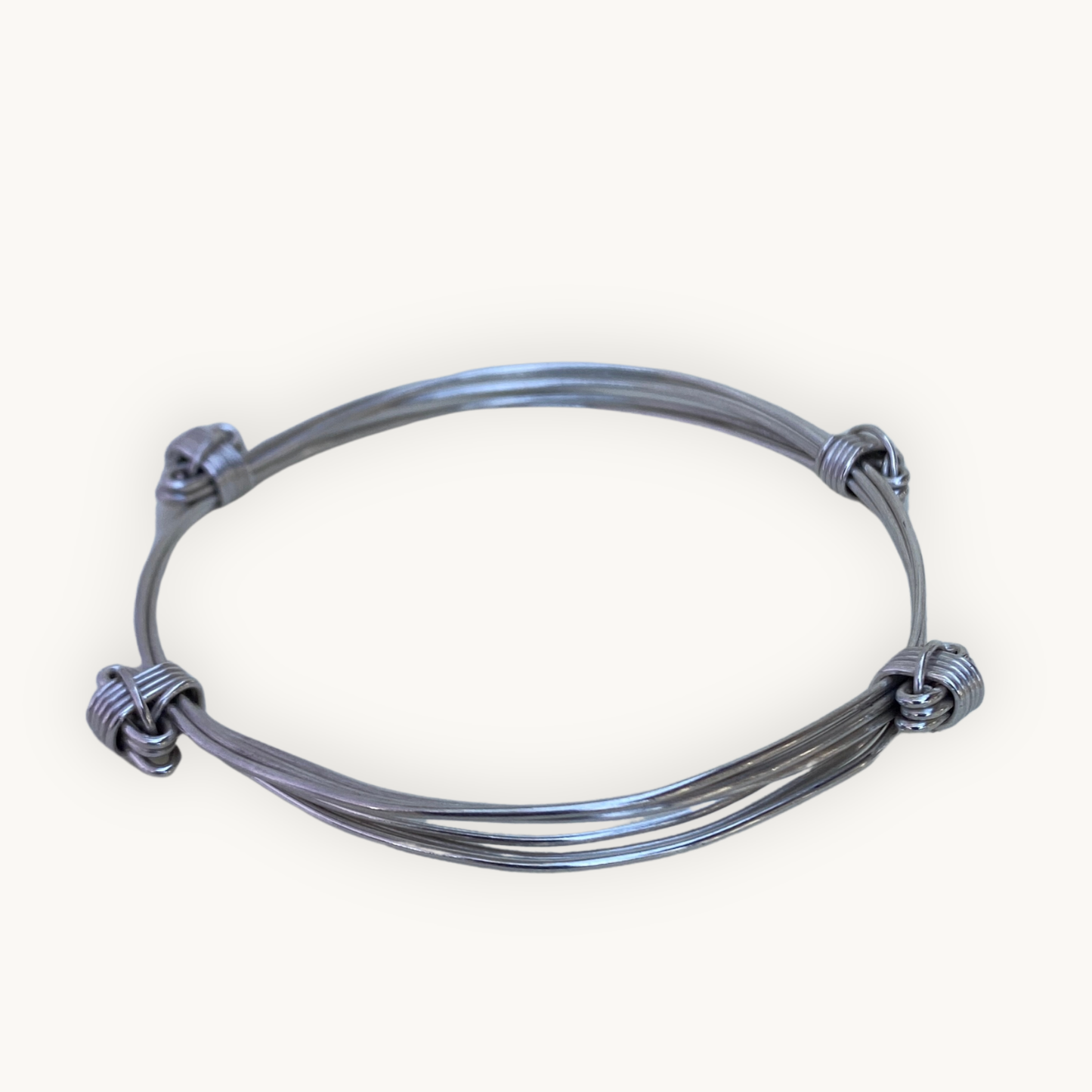 Angled view of a handcrafted sterling silver four knot three strand Elephant Knot bangle on a white background.