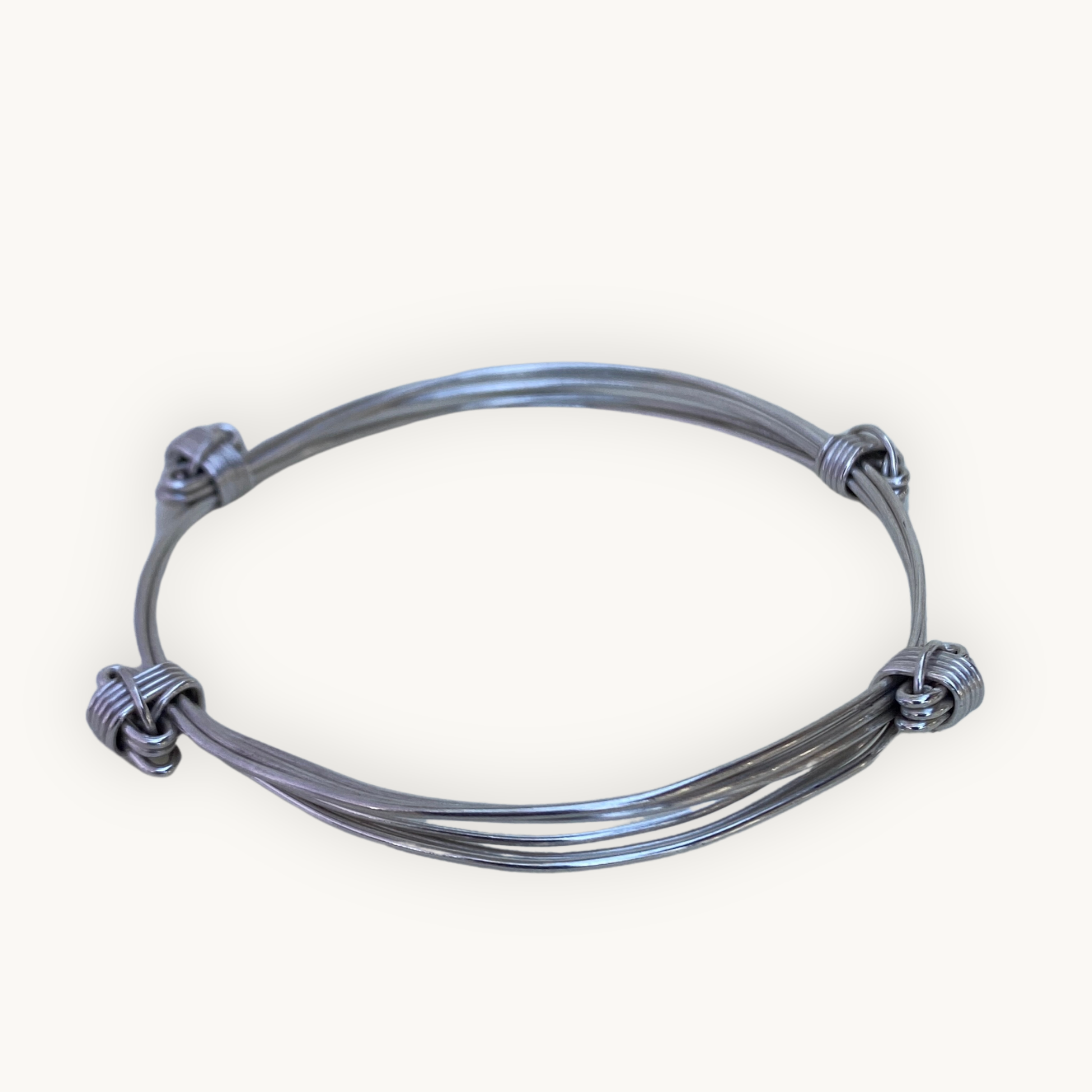 Angled view of a handcrafted sterling silver four knot three strand Elephant Knot bangle on a white background.