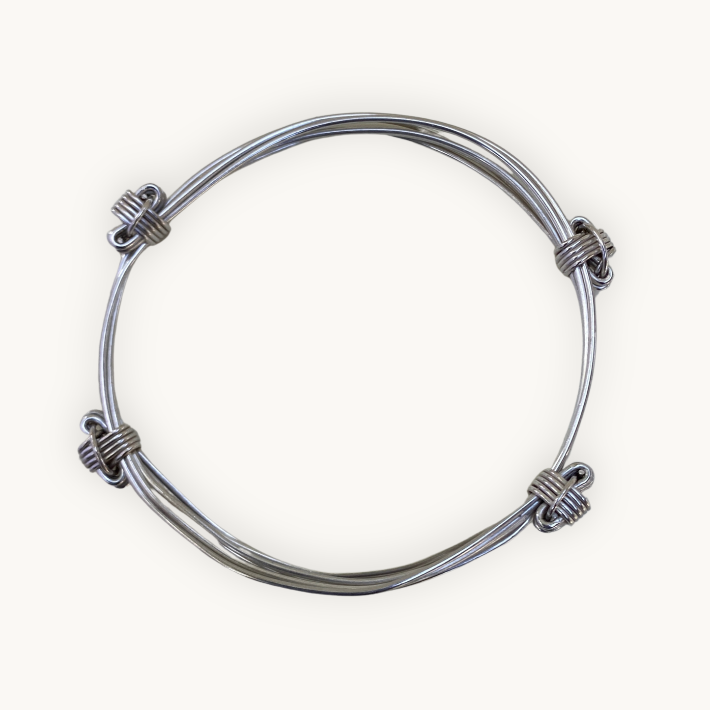 Top view of a handcrafted sterling silver four knot three strand Elephant Knot bangle on a white background.