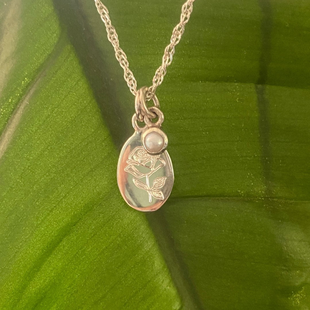 Handcrafted sterling silver birth flower necklace with gemstone displayed on a tropical green leaf.
