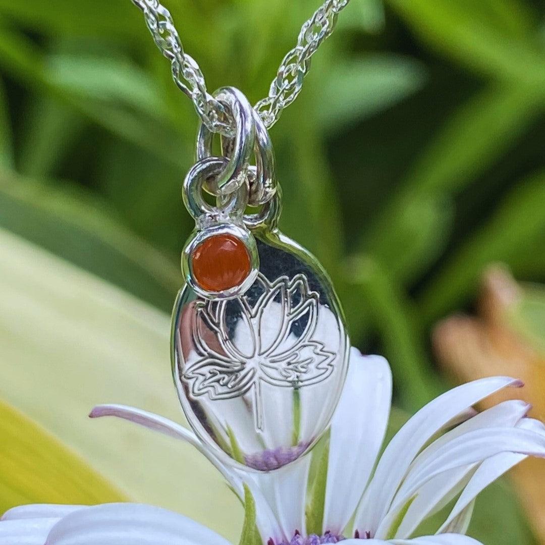 Handcrafted sterling silver birth flower necklace with red gemstone displayed on a white flower.