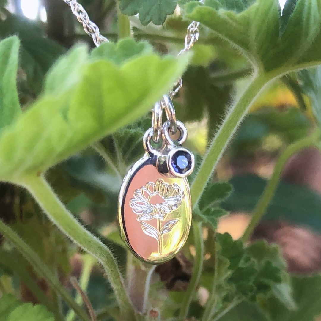 Handcrafted sterling silver birth flower necklace with pink gemstone displayed on a white flower.