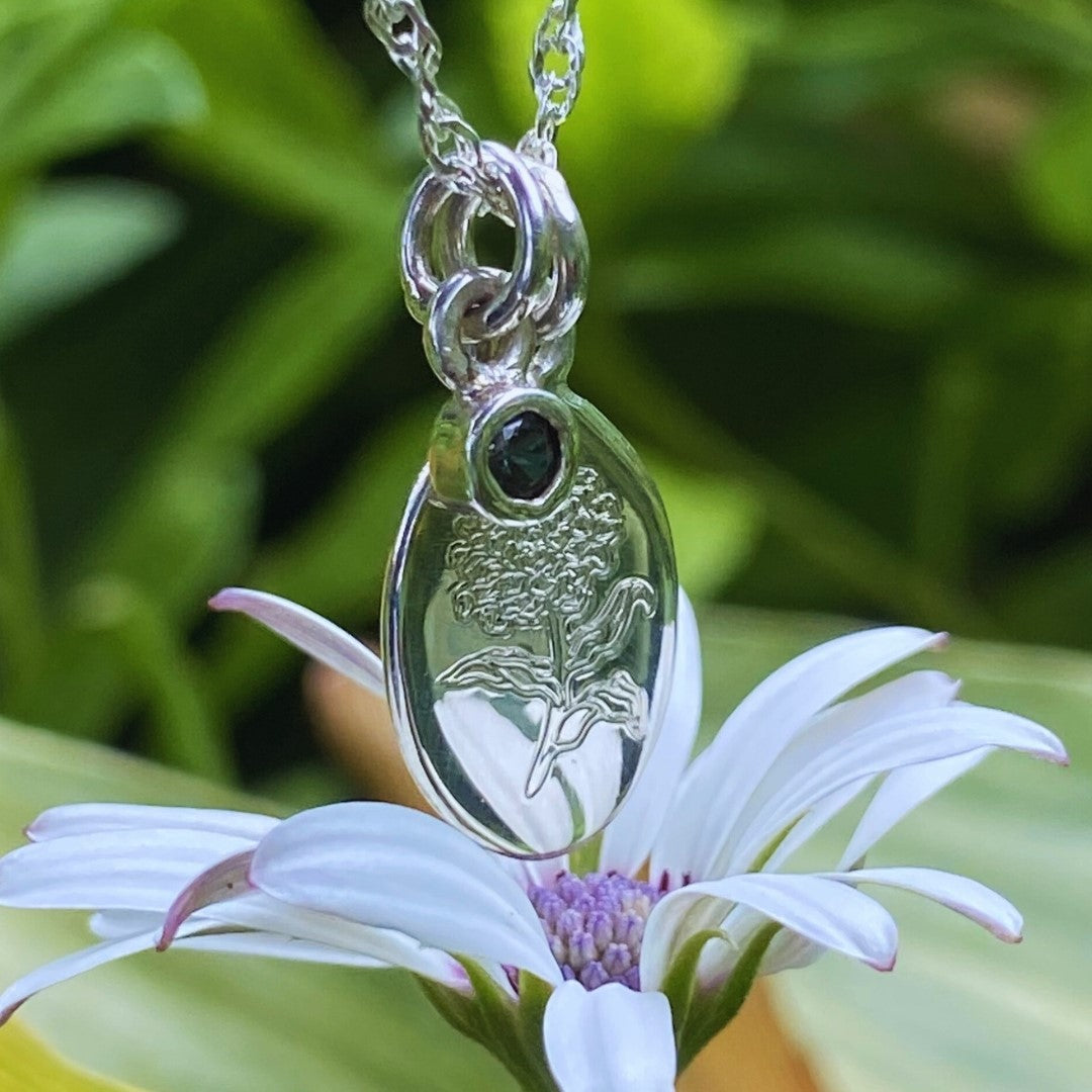 Handcrafted sterling silver birth flower necklace with yellow gemstone displayed on a tropical green leaf.