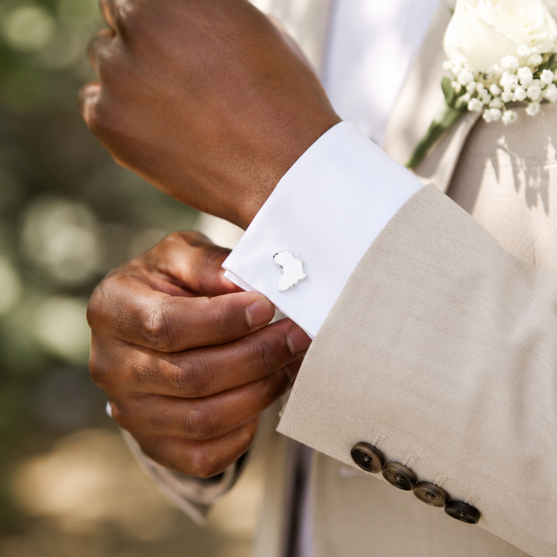 A man wearing a wedding suit adjusting his cuff on which he has silver African Cufflinks