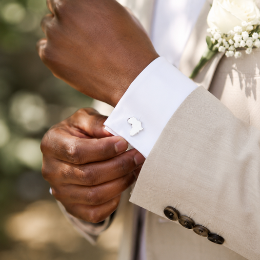 A man wearing a wedding suit adjusting his cuff on which he has silver African Cufflinks